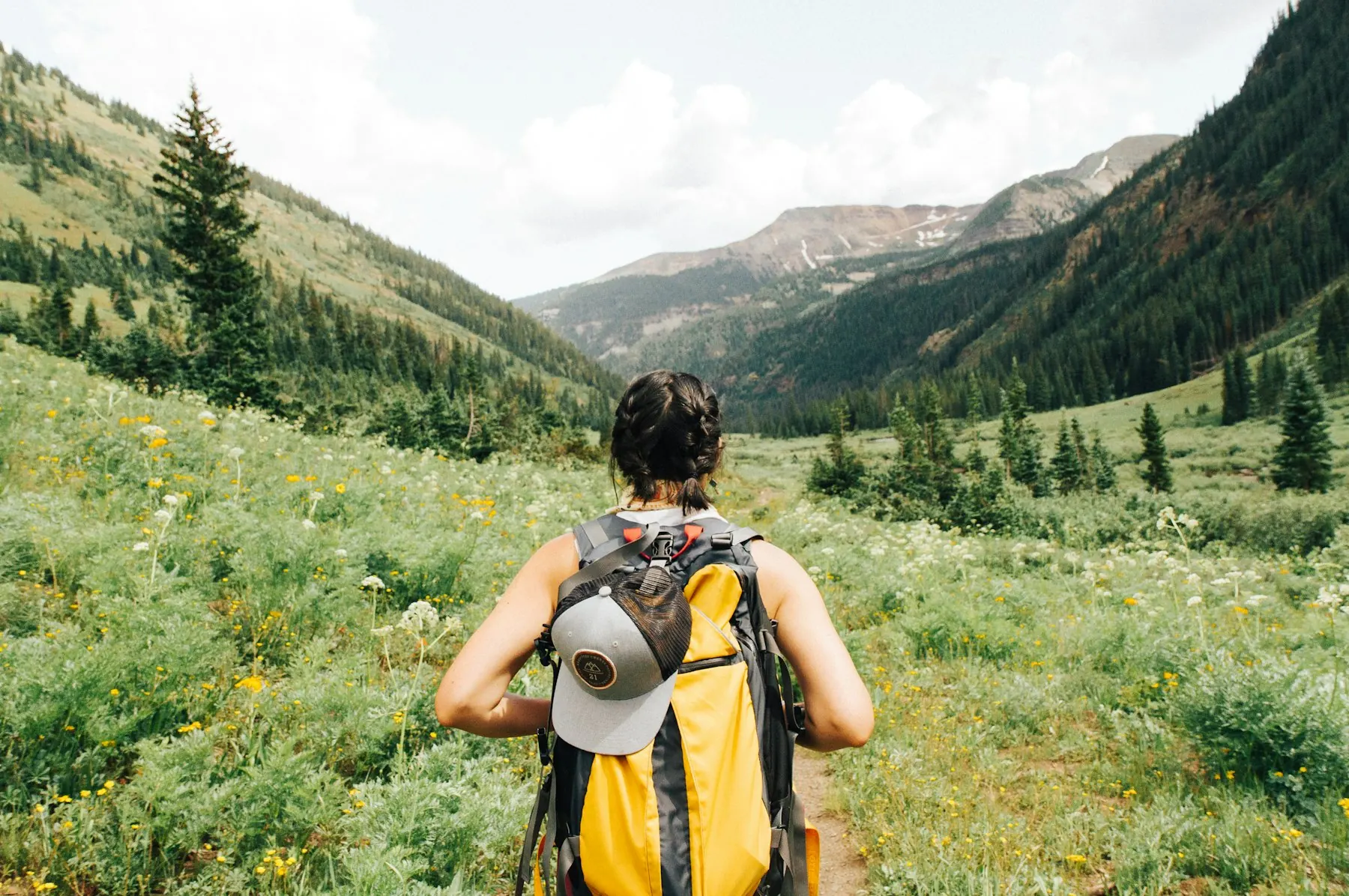Hiker with a yellow backpack walking through an alpine valley